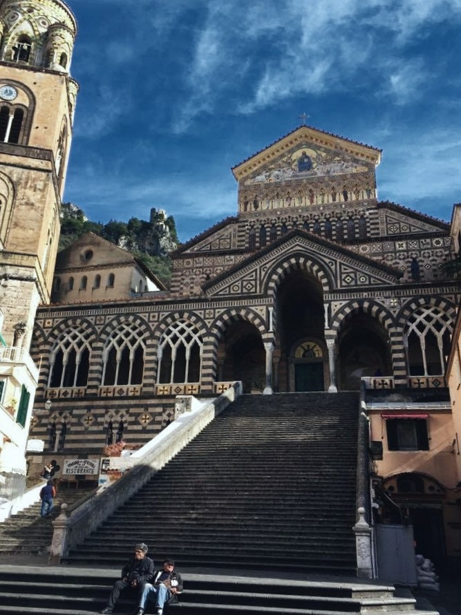 The golden facade of the Amalfi Cathedral (Duomo di Amalfi) under dramatic winter storm clouds in Amalfi, Italy.