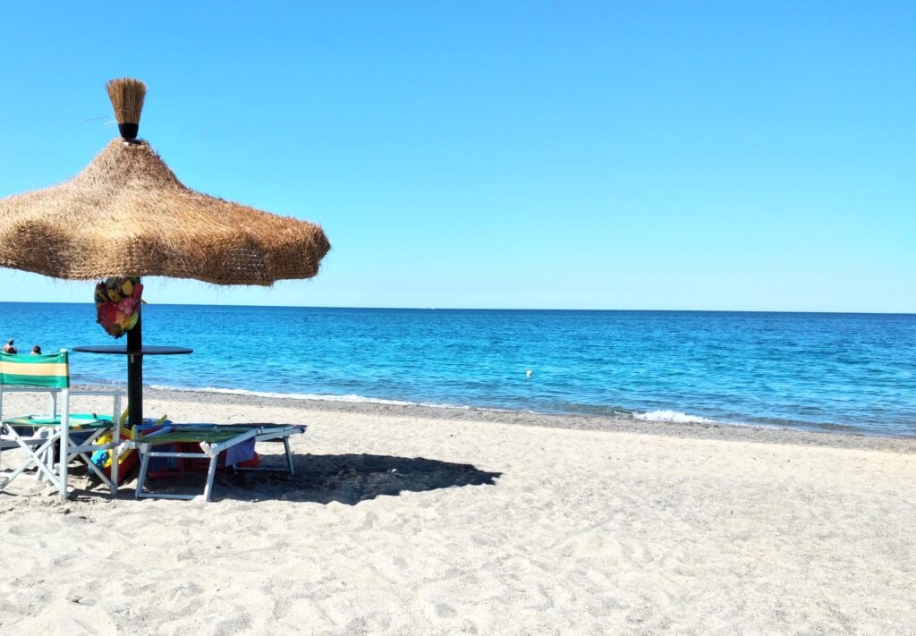 A serene morning on an empty sandy beach in Cilento, Italy, featuring a single umbrella, crystal-clear blue sea water, and a Blue Flag award.